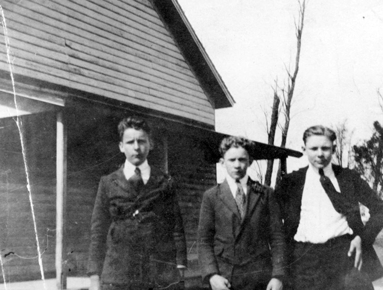Black and white photograph of three boys standing in front of the Groveton School. They are dressed formally with white shirts, ties, and dark jackets.