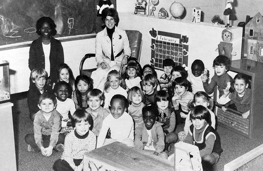 Black and white photograph from Groveton Elementary School's 1975 to 1976 yearbook showing students and teachers in the Apple Blossom kindergarten morning class. The children are seated on the floor in a classroom, and two teachers, sitting in chairs, are at the back of the group. 23 children are pictured.