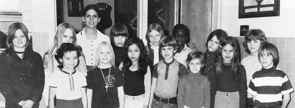 Black and white photograph of Groveton Elementary School's Cafeteria Committee from the 1973 to 1974 yearbook. 14 children and one adult are pictured. They are standing inside the cafeteria near a doorway.