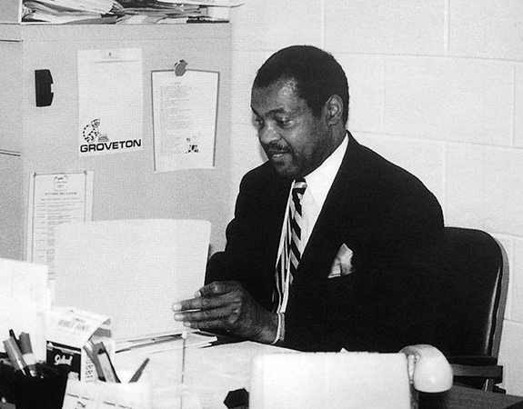 Black and white photograph of Principal Thompson seated at his desk. He is looking through paperwork.