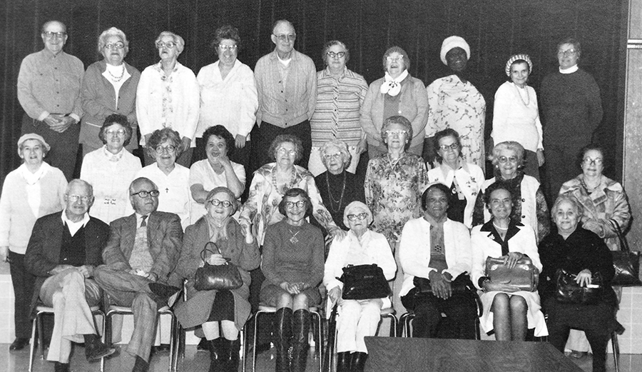 Black and white photograph of some of the senior citizens who took part in the nutrition program during the 1980 to 1981 school year. 28 people are in the picture. They are arranged in three rows on, and in front of, the school's stage.