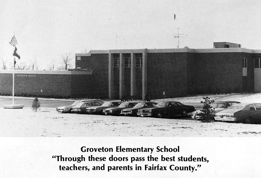 Black and white photograph of Groveton Elementary School from the 1974 to 1975 yearbook. There is a light covering of snow on the ground. The original main entrance to the building is pictured. The entrance was moved during a subsequent renovation. The photograph has a caption that reads: Groveton Elementary School - Through these doors pass the best students, teachers, and parents in Fairfax County.