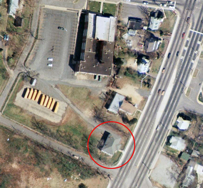 Color aerial photograph taken in 1976. The two Groveton schools can be seen from directly overhead. The two-room school is at the bottom of the picture, and the large brick school is at the center top of the picture. Along Route 1, next to both schools, are several houses and a church. A gravel walkway leads from the parking lot of the brick school to the frame building. Several school buses are parked in the lot behind the elementary school. Route 1 has been widened to three lanes in both directions.