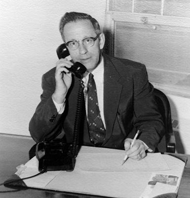 Black and white photograph of Principal Day from a collection of Virginia Hills Elementary School memorabilia. He is seated at his desk and is talking on the phone.